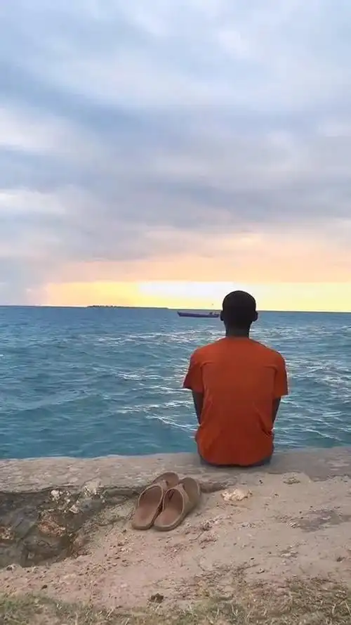 小伙坐在海边欣赏风景夕阳西下海水湛蓝