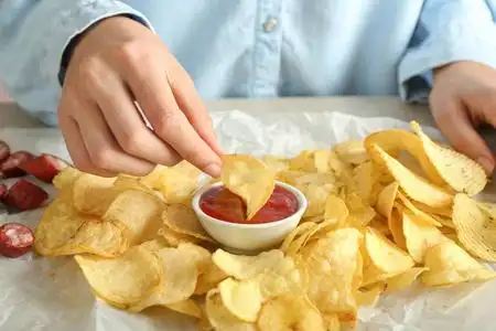 女人吃美味的薯片加番茄酱特写照片