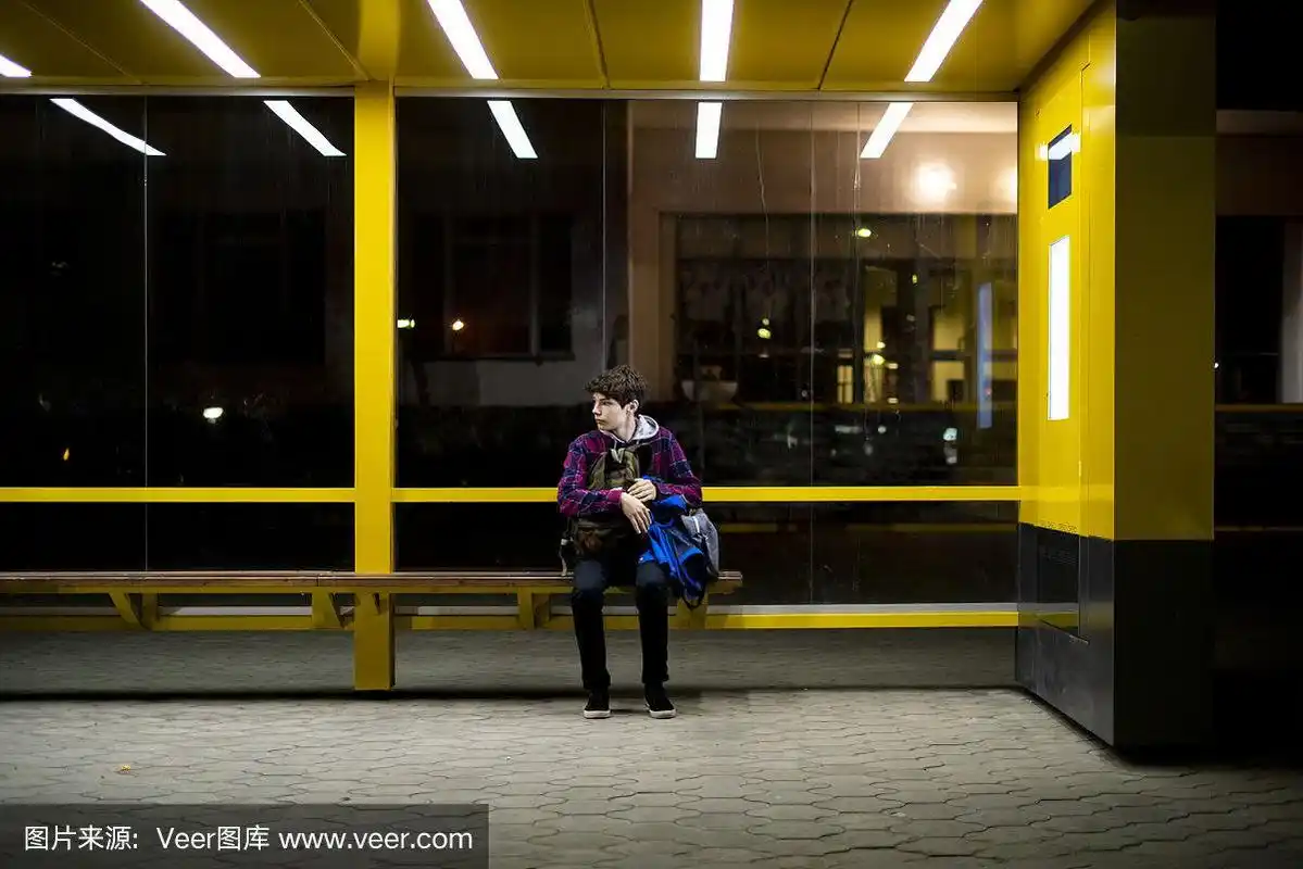 一个年轻人晚上坐在公交车站的长椅上等车