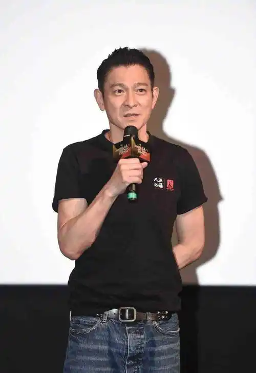 视频中刘德华身着黑色短袖t恤,蓝色牛仔裤,黑色休闲鞋,梳着黑亮的大