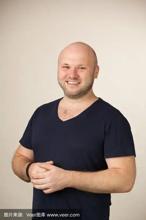 一名35岁剃着光头的大胡子男子的工作室肖像,他穿着一件蓝色t恤,米色