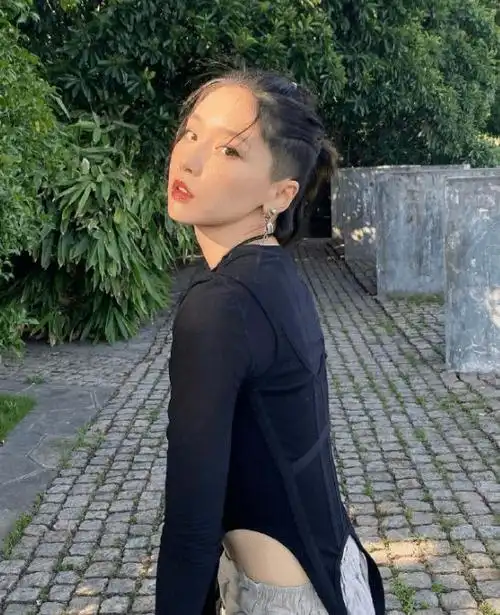 照片中的她剃光一边鬓角的头发,其余头发梳起来扎成小辫,身着黑色不