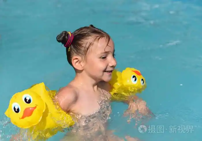 一个阳光明媚的享受玩和在游泳池里打开一个微笑的小女孩照片