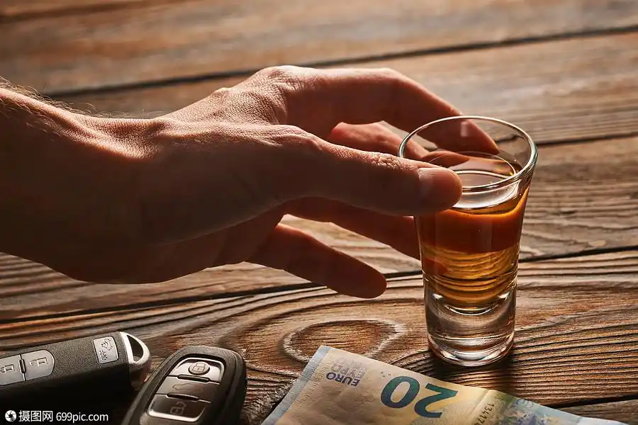 男人的手伸向乡村木桌上的杯龙舌兰酒精饮料汽车钥匙喝酒开车酗酒的