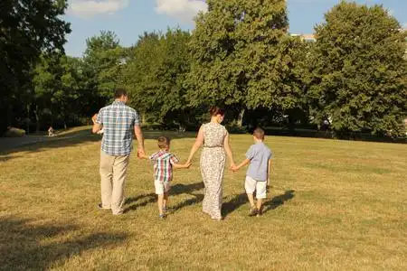 一男一女穿着夏装,两个儿子和一个抱着小孩的爸爸正走在公园里,一个