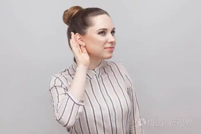 穿着条纹衬衫,收集着禁止的发型,手靠近耳朵站着,试图倾听