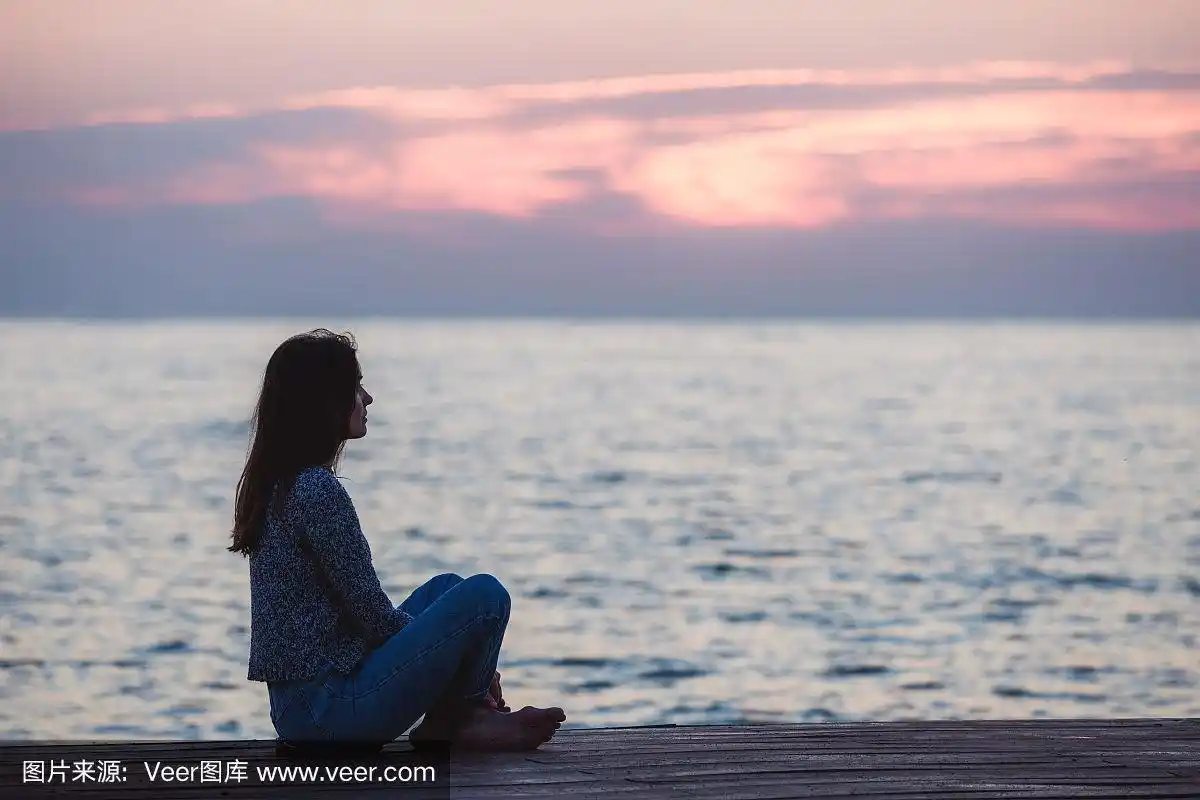 孤独的女孩坐在日出的海滩上