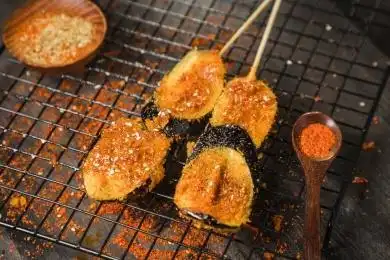 黑色烤架上放着两串撒着辣椒面油炸茄子片