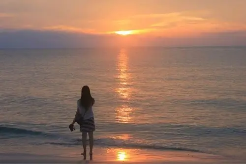 一个女孩蹲在夕阳下的沙滩上拿着相机拍照 求图!