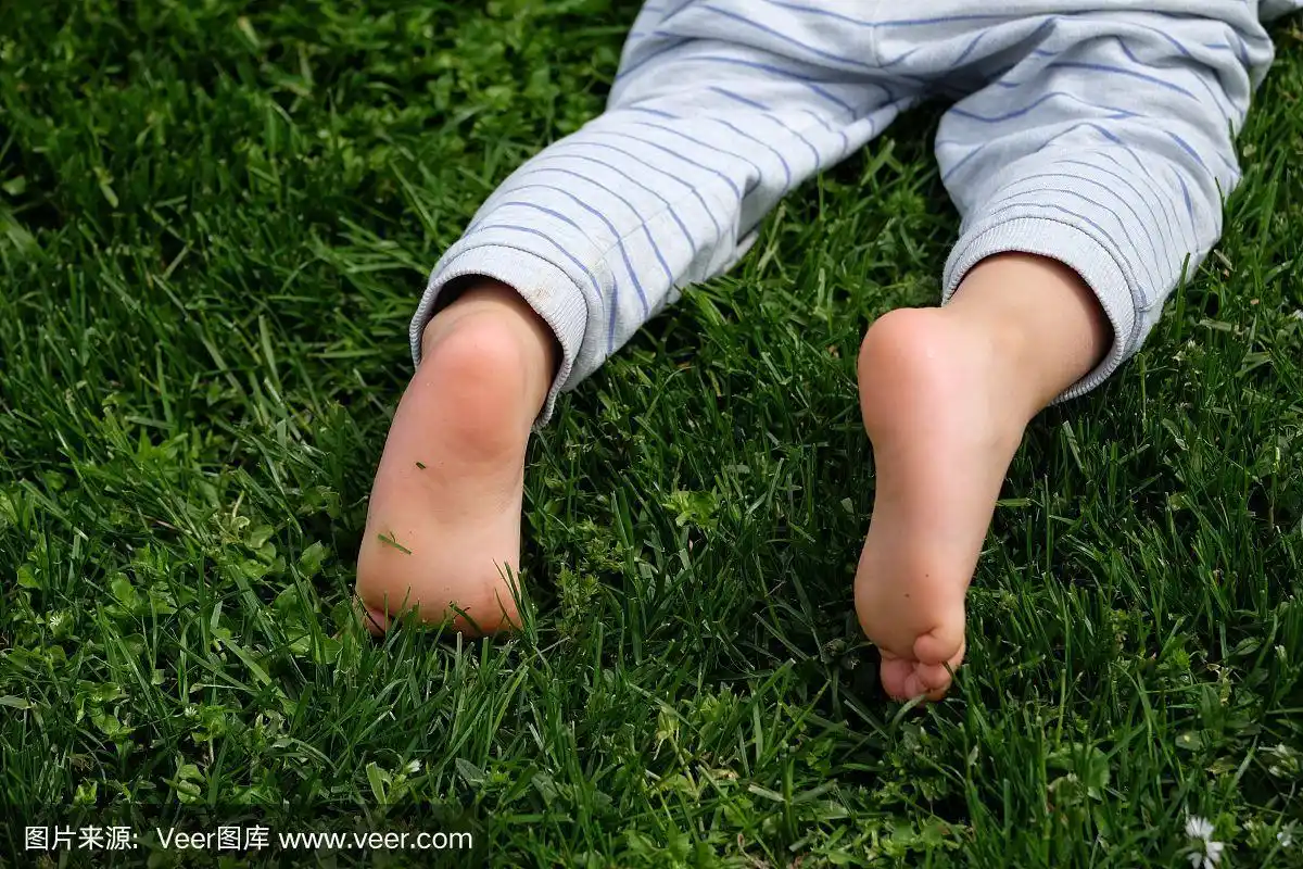 婴儿赤裸的脚在绿色的草地背景孤立在绿色的背景上的特写.