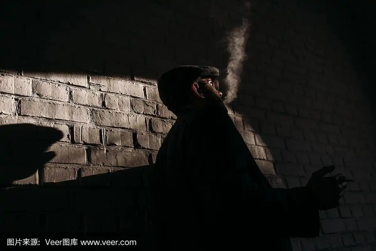 在砖墙前抽烟的时髦男子的剪影