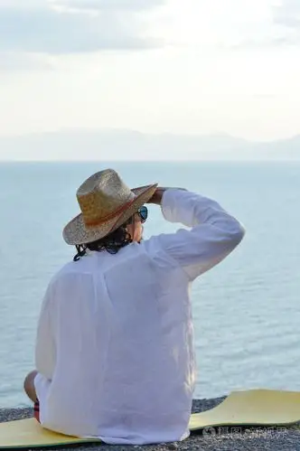 坐在海边沙滩上的白色衬衫凉帽的男人