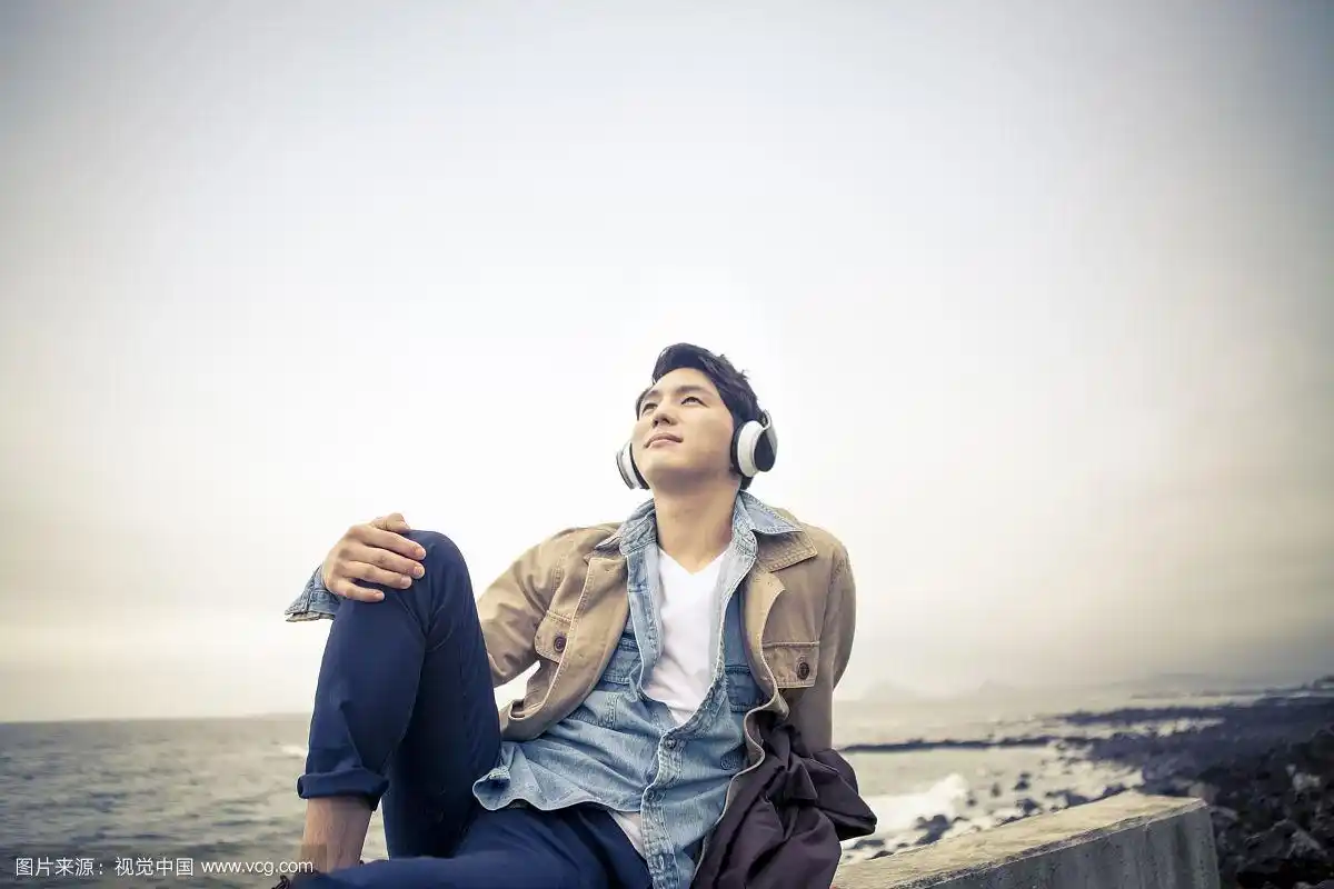 一个人坐在海边用耳机听音乐的照片