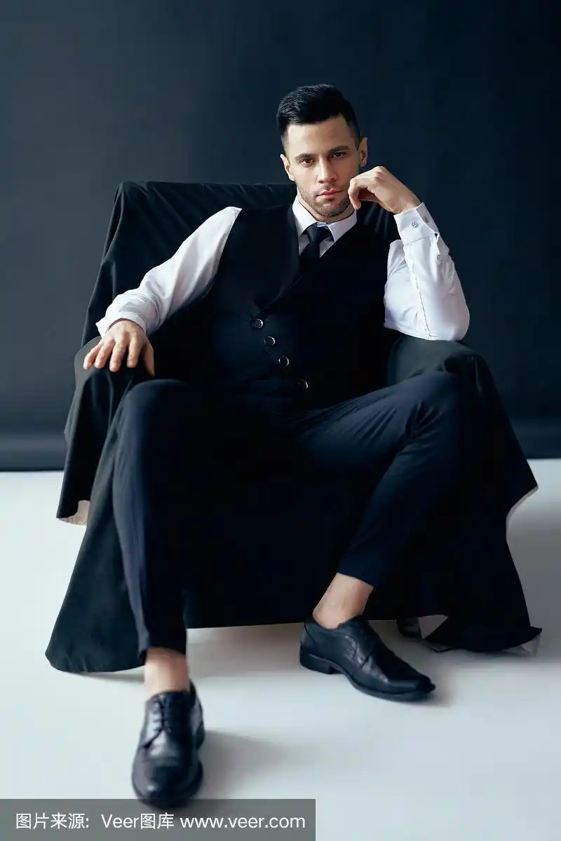 自信周到的男人在优雅的西装摆姿势坐在椅子上