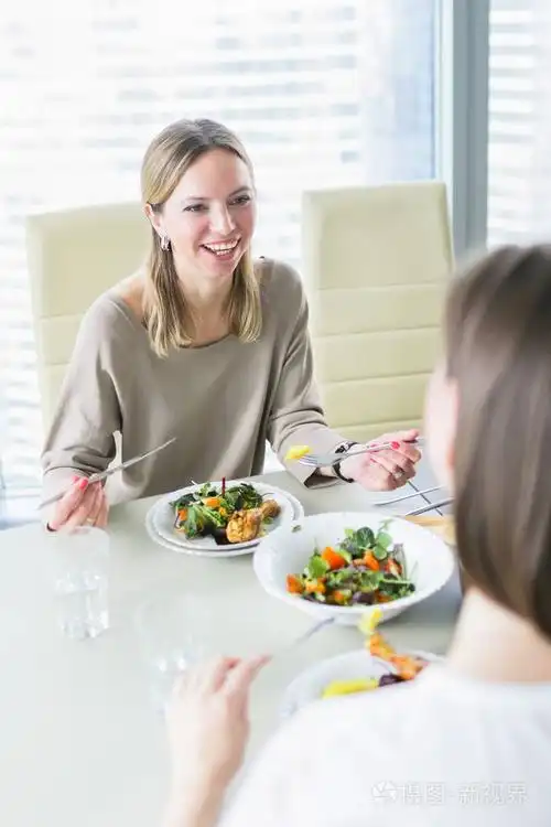 微笑的女人一起在窗前的现代厨房的桌子前吃饭照片-正版商用图片0zmw0