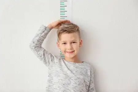 小男孩测量高度在轻的墙壁附近照片