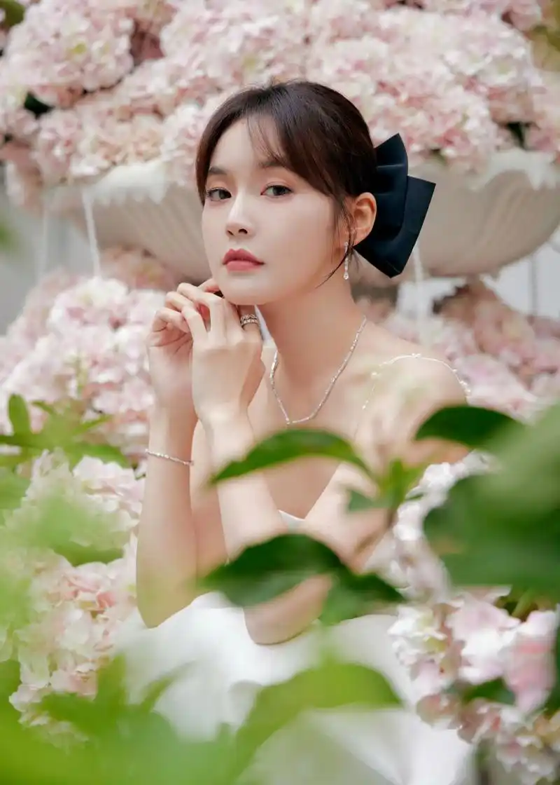 粉花丛中,张佳宁身穿白色连衣裙,头戴黑色蝴蝶结,优雅又甜美.