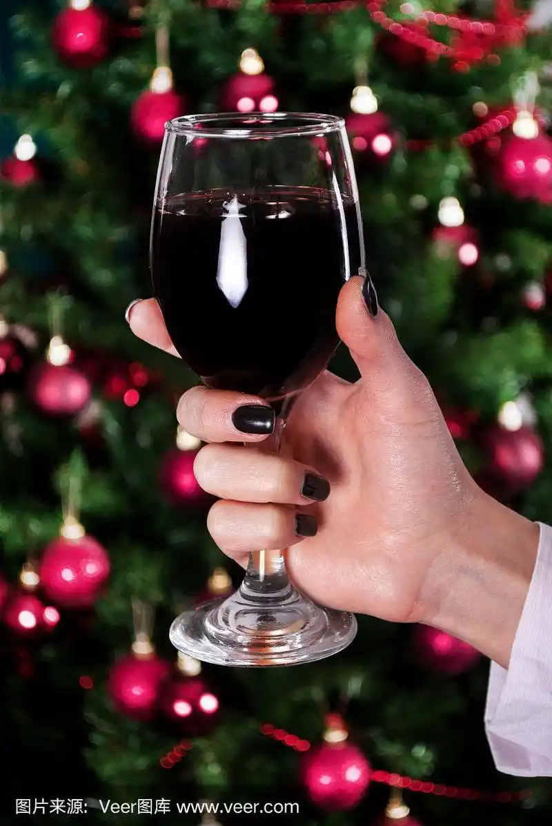 红酒杯在年轻女孩的手和装饰圣诞树的背景