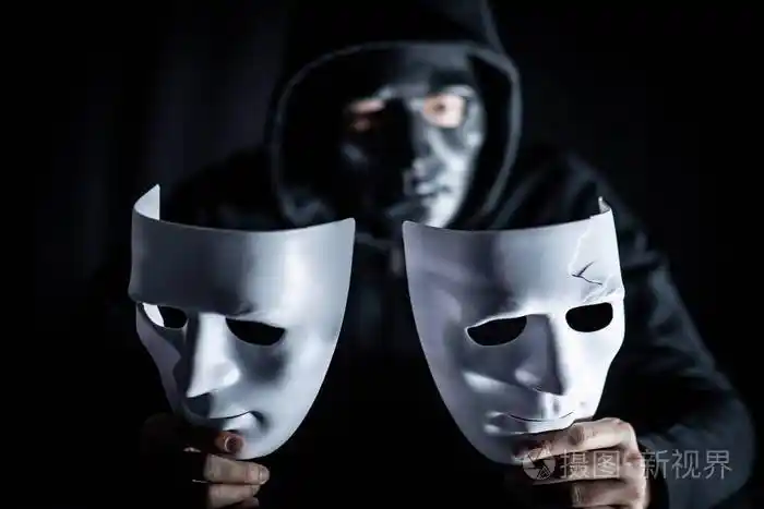 神秘的帽衫人戴着黑色面具, 手里拿著两个白面具.匿名社交屏蔽.