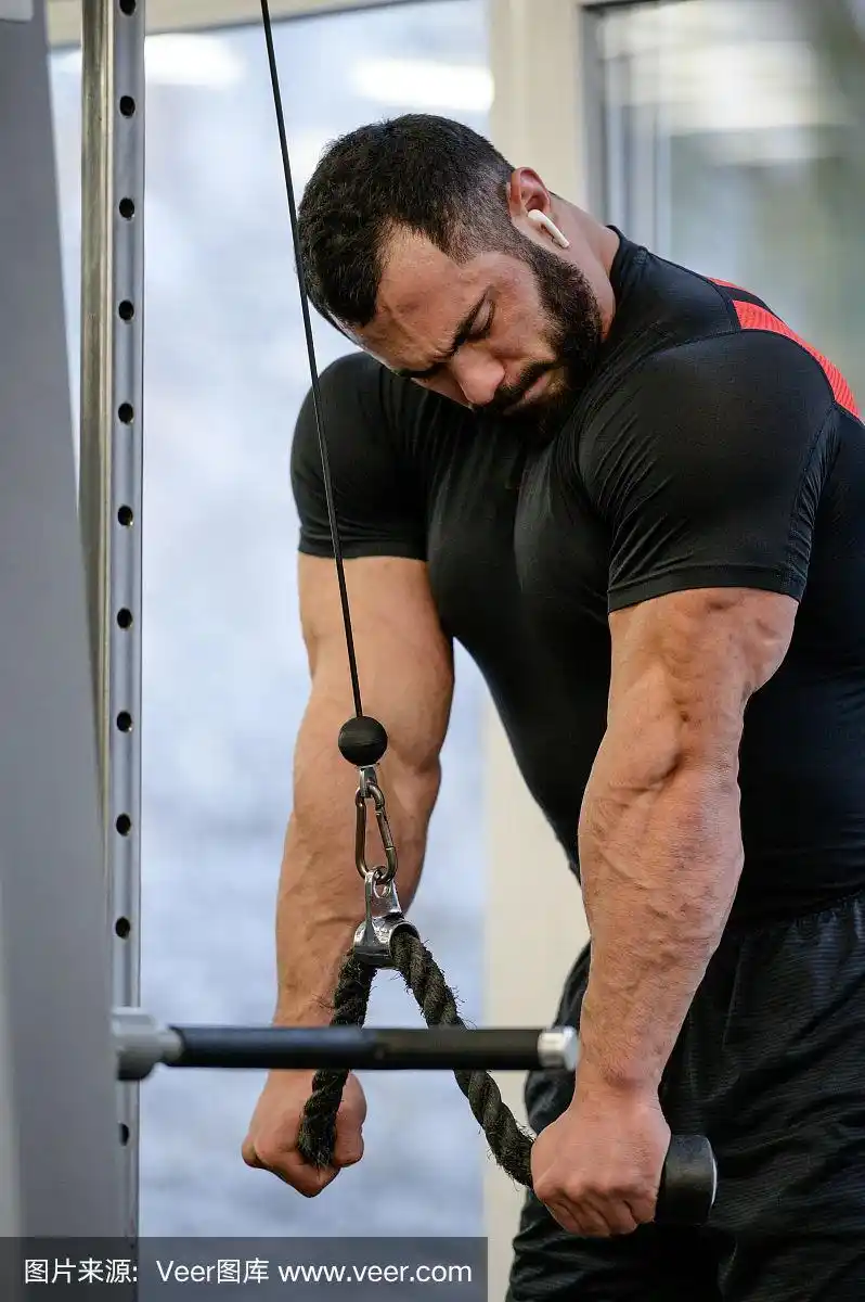 强壮健康的年轻留胡子的运动男子在黑色运动服和无线耳机在锻炼肌肉三