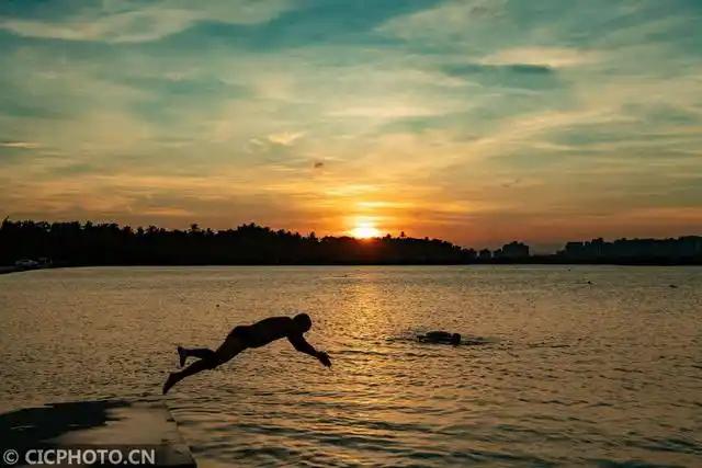 2021年5月13日,在海南省琼海市,市民在美丽霞光下的万泉河上游泳