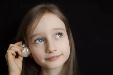 贝壳的旁边可爱的金发女孩微笑着拿着贝壳在她的耳朵旁边,听在黑色