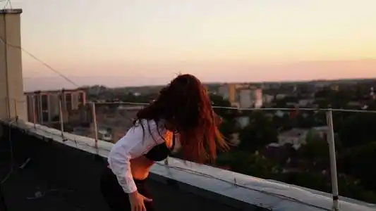 日落时,穿着运动服的年轻女孩坐在屋顶的边缘.照片