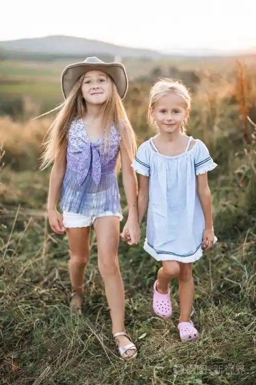 女孩姐妹或朋友一起走在田野或草地上手牵手户外可爱小孩的肖像夏天