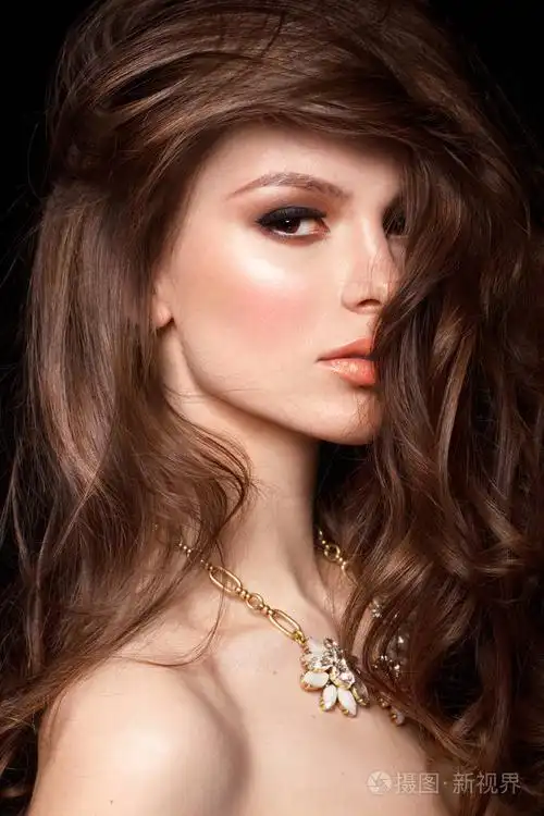 时尚黑发女人的美丽的肖像与波浪头发穿着金色的项链与花卉设计在黑色