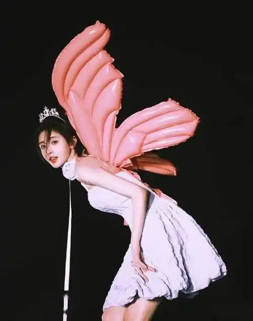 照片中,鞠婧祎穿着粉紫色连衣裙,头戴皇冠,背着粉色充气翅膀,身材纤细