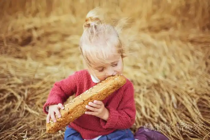 一个漂亮的小女孩在一个字段上吃面包