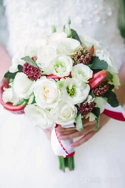 美丽的女人手拿玫瑰鲜花花束,外面的白色的婚纱礼服.