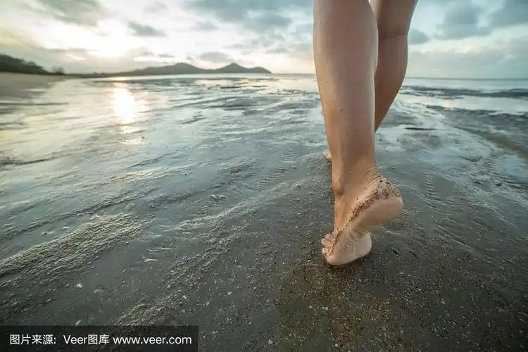 在太阳升起时赤脚在海滩上行走的特写