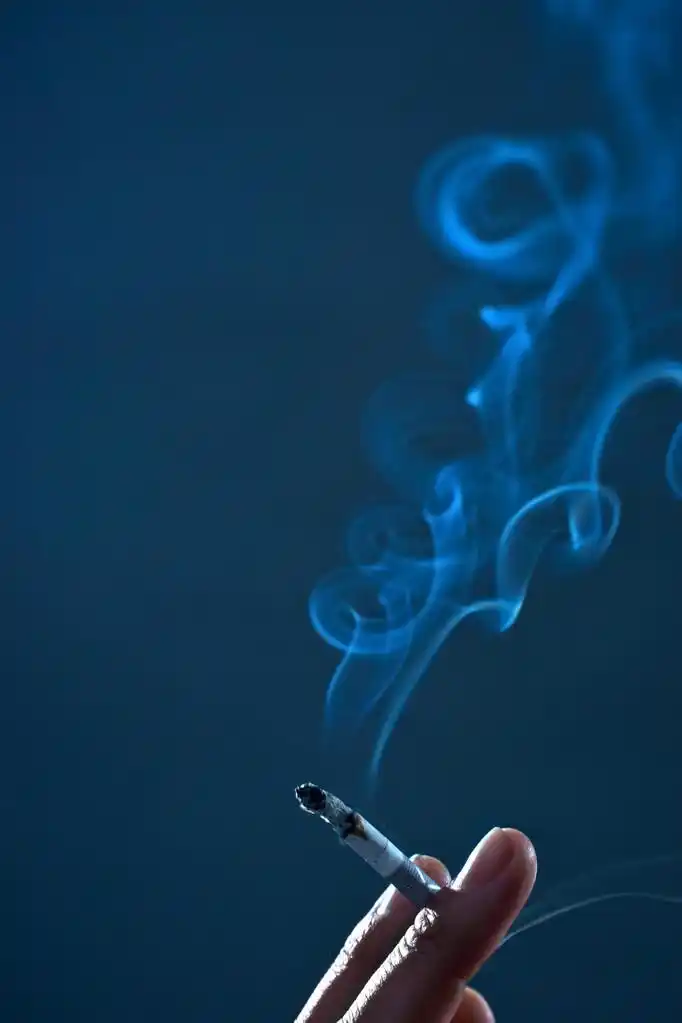 抽着烟,在暗蓝色背景上的一只手抽香烟