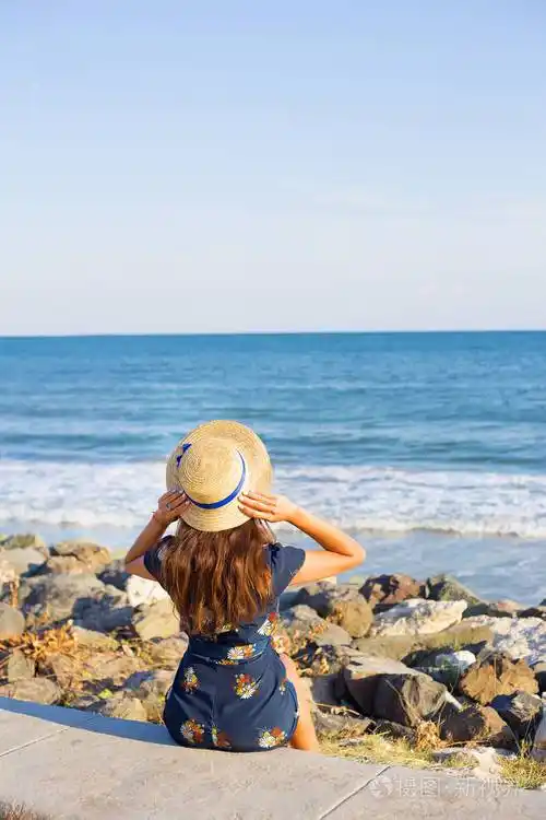 美丽的女孩在一顶帽子在海边坐在石头上照片-正版商用图片050c6t-摄图