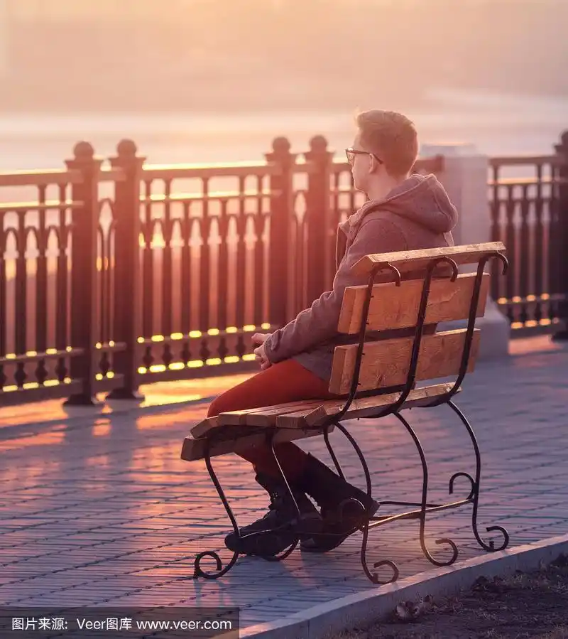 孤独的男人坐在长椅上,夕阳西下
