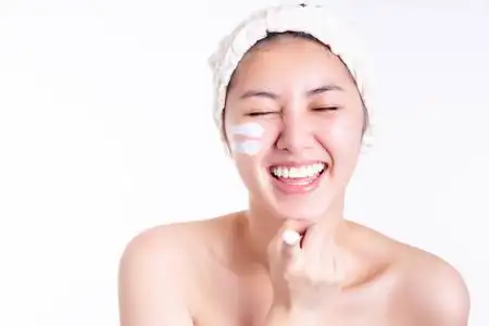 年轻女子展示面霜,润肤霜在脸上,手指上.微笑的亚洲美女得到幸福.