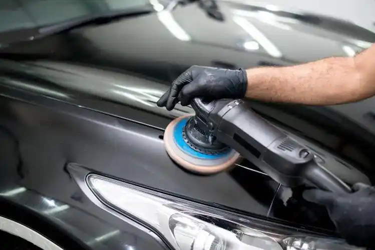 工人手持工具给黑色汽车做抛光