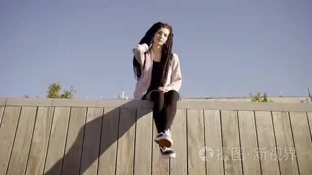 年轻的女孩坐在屋顶上倒挂在黑色紧身裤和运动鞋.