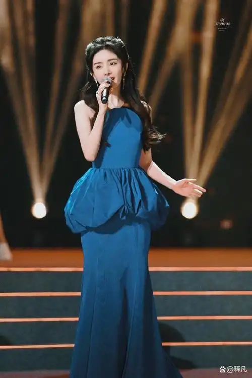 俏脸清丽,秀眸明亮,扎公主头,她单手拿着话筒演唱歌曲,气质优雅端庄