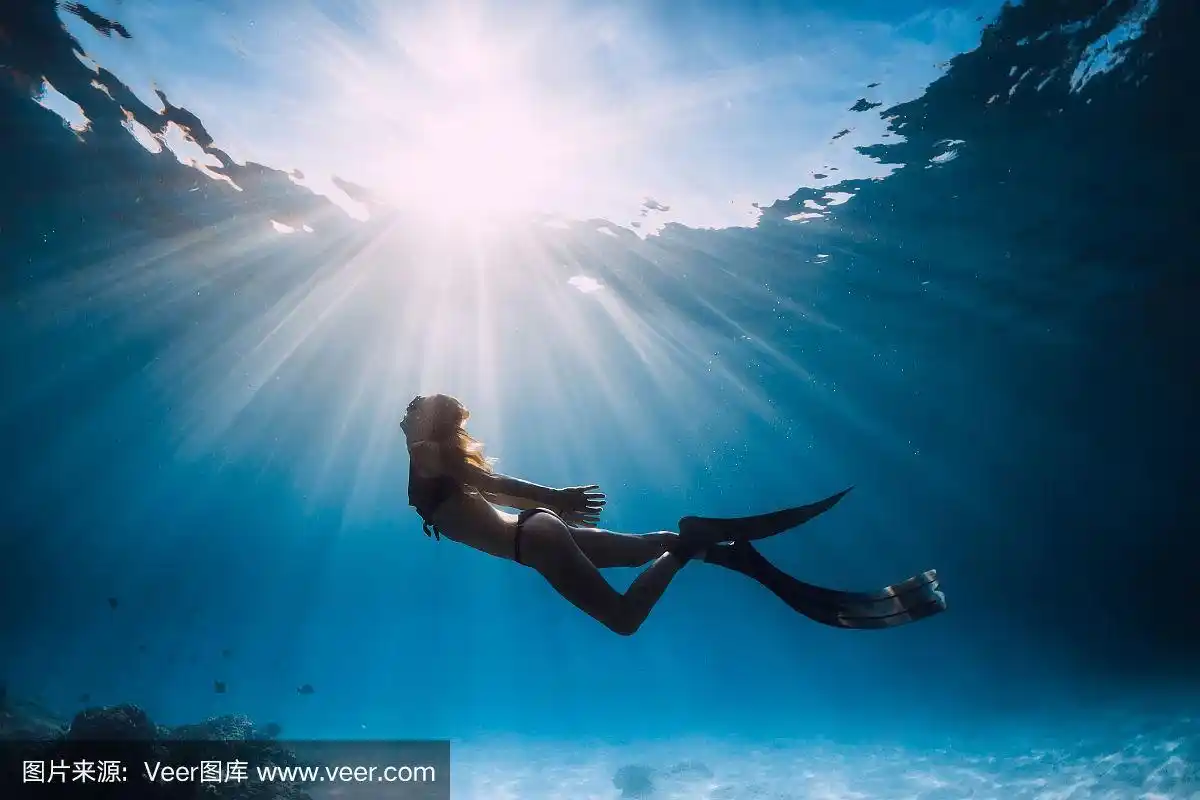 女自由潜水者与鳍游泳在沙滩和阳光水下