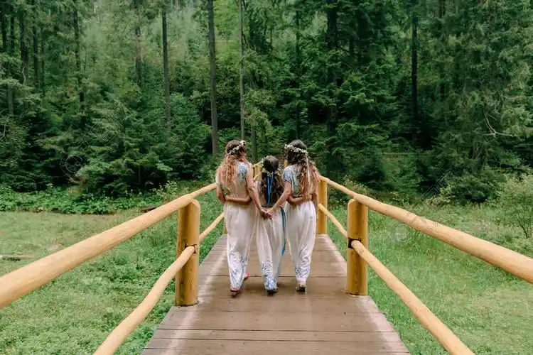 妈妈和两个女儿穿着白色裙子着花环的野花在湖边散步