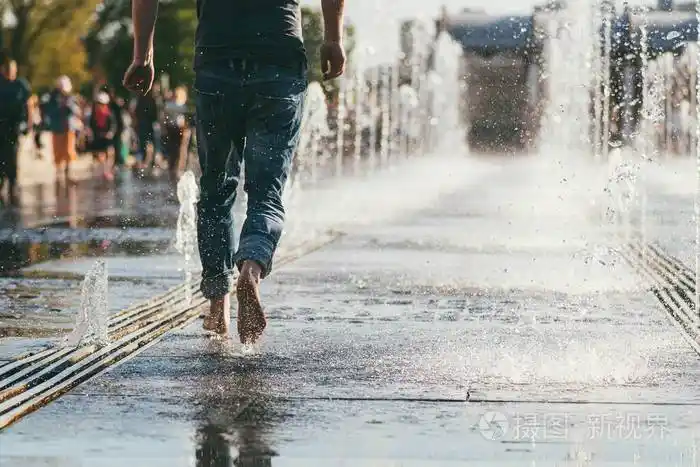 一个穿着牛仔裤的男人赤脚在城市喷泉的溪流之间奔跑的中间图