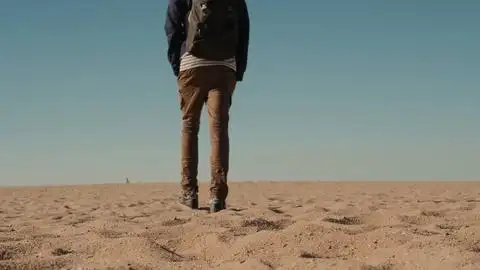 一个人独自走在迪拜附近阳光明媚的沙漠里背包旅游