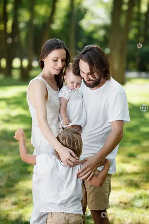 甜蜜美丽的家庭正在公园里放松.爸爸妈妈抱着女儿抱着儿子