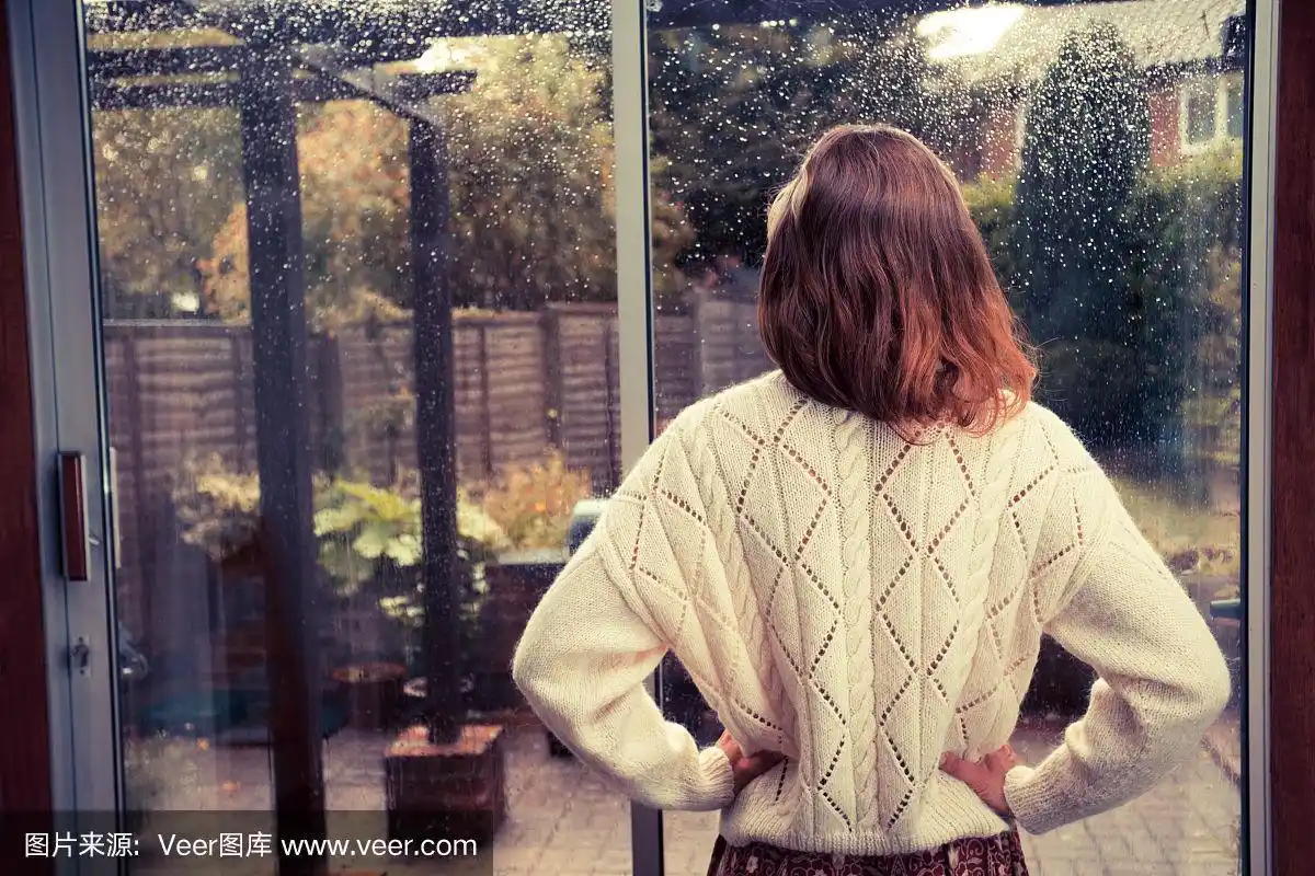 年轻女子在窗前看雨