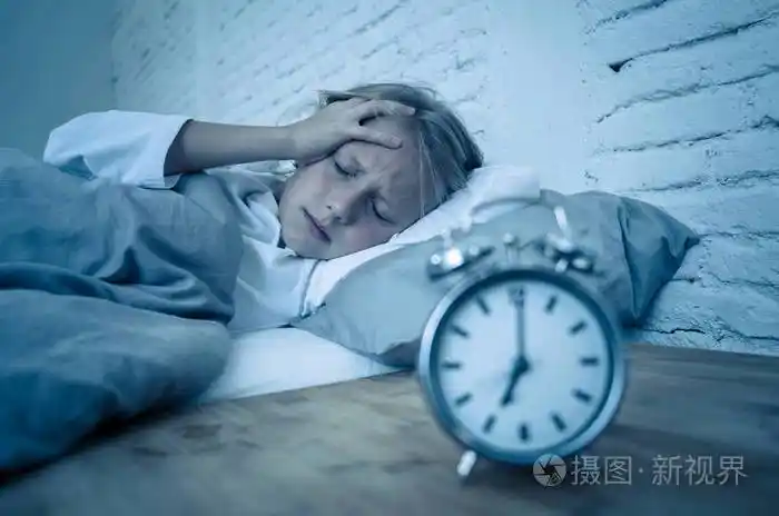 甜蜜的失眠小女孩躺在床上悲伤地看着闹钟,不得不醒来,但在烦恼中感到