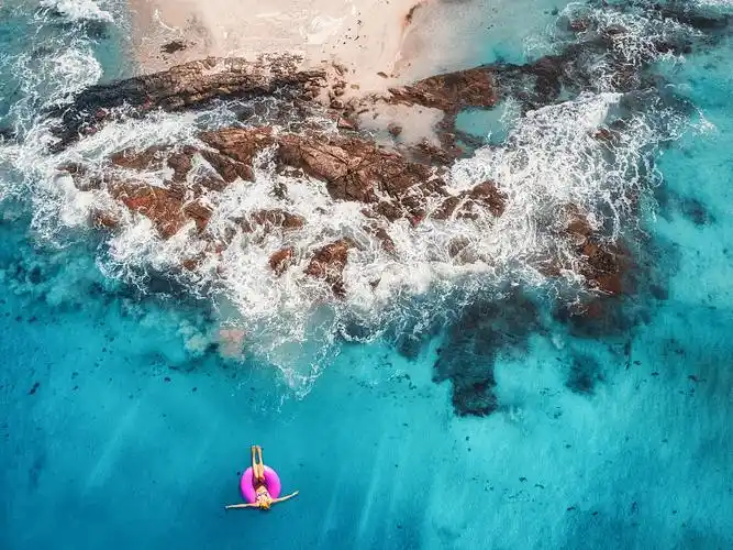 夏天的海景与女孩,海滩,美丽的海浪,岩石,蓝色的水在日落.前视图.