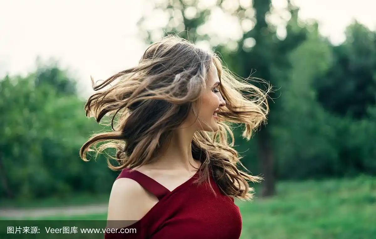 年轻快乐的女人与飘动的头发有乐趣户外在绿色的夏季自然背景