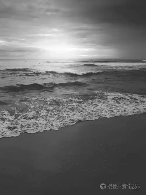 在平静的海浪和沙滩上日出的黑白风景